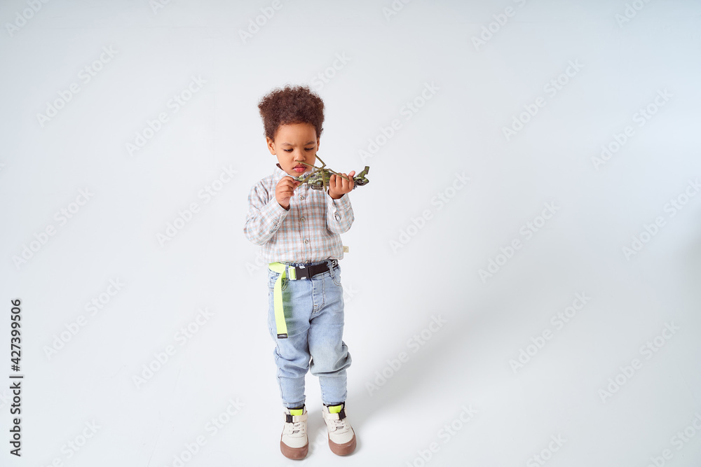 Little African-American boy sits with toy helicopter on white background