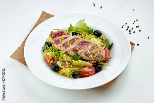 Appetizing and healthy salad with grilled tataki tuna steak, tomatoes and olives, served in a white plate. white background. Close up, selective focus