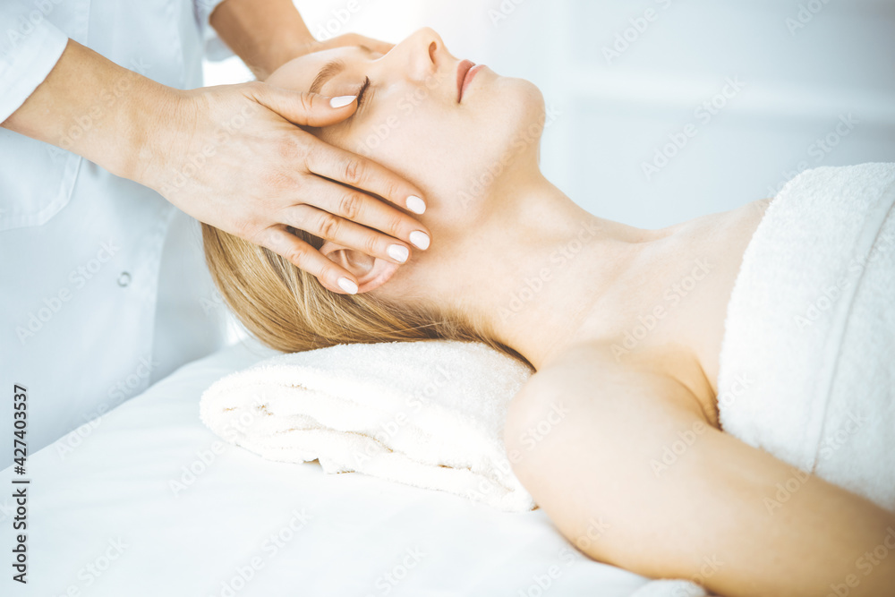 Happy woman enjoying facial massage with closed eyes in spa salon. Relaxing treatment in medicine and Beauty concept Happy woman enjoying facial massage with closed eyes in spa salon. Relaxing treatment in medicine and Beauty concept