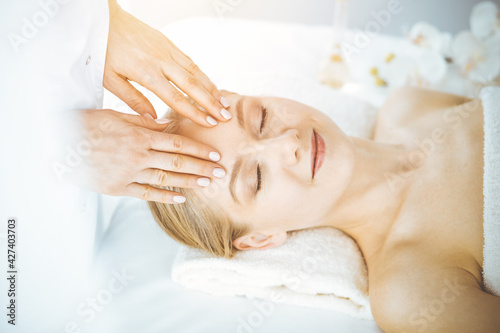 Beautiful caucasian woman enjoying facial massage with closed eyes in spa salon. Relaxing treatment in medicine and Beauty concept © Iryna