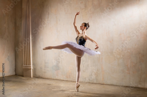 Young ballerina in white tutu dancing in a spotlight in vintage scene