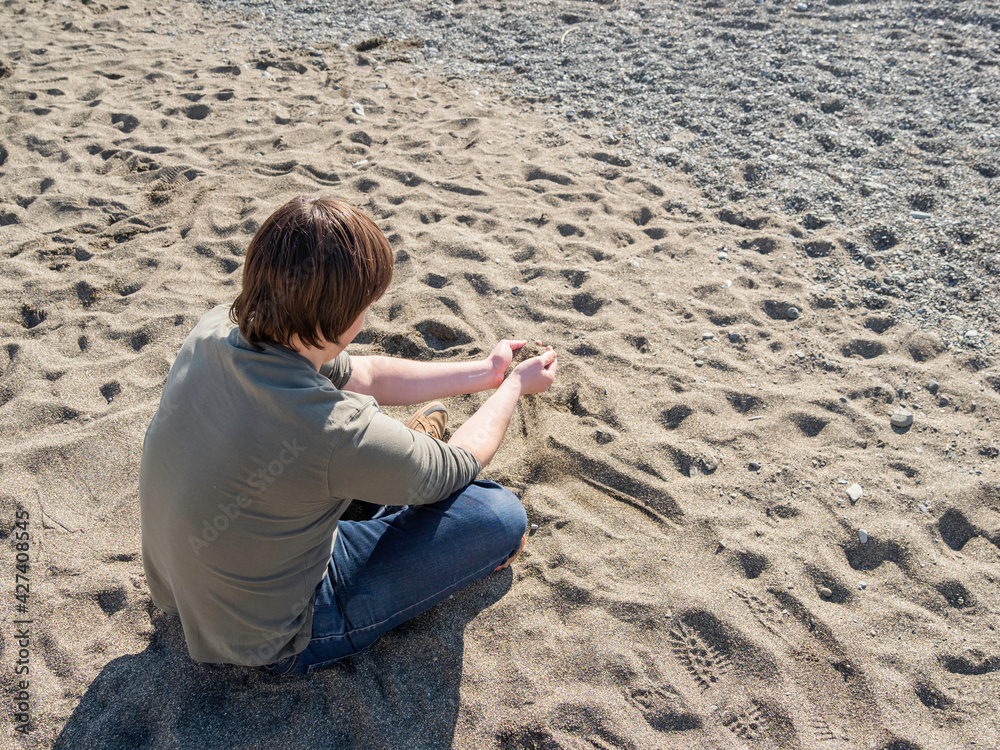 Man relaxes on sandy beach and pours sand from hand to hand. Peaceful leisure activity at warm season. Sunny day at seaside.