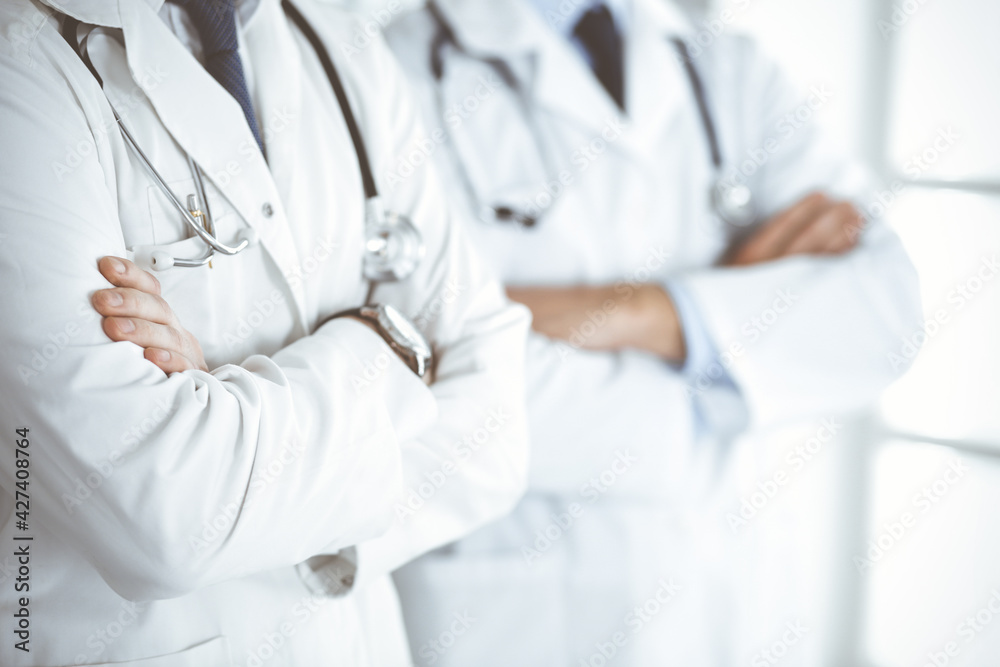 Group of unknown doctors standing as a team with arms crossed in hospital office, close-up. Medical help, insurance in health care and medicine concept Group of unknown doctors standing as a team with arms crossed in hospital office, close-up. Medical help, insurance in health care and medicine concept
