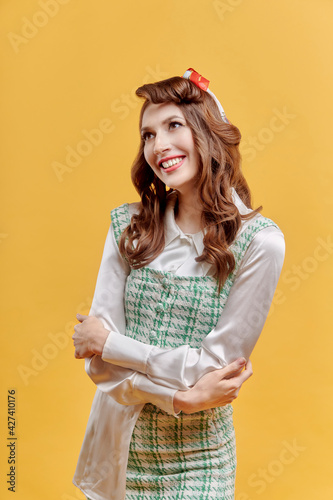 Happy young beautiful brunette woman with wavy hair, bow on her head. Pin-up style. Yellow background.