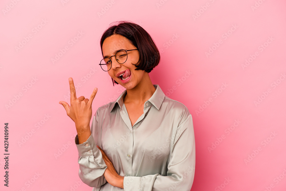 Young mixed race woman isolated on pink background showing rock gesture with fingers Young mixed race woman isolated on pink background showing rock gesture with fingers