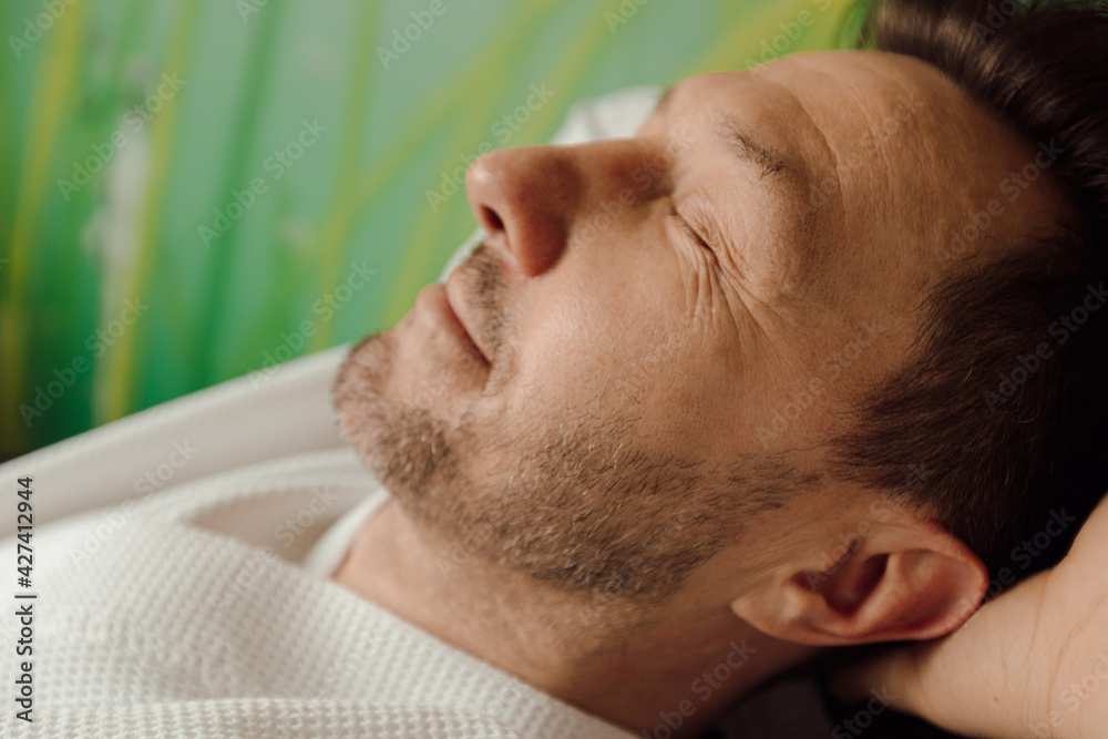 Obraz premium Close up face portrait handsome smiling man enjoying free time in bathrobe with closed eyes. spa relaxation