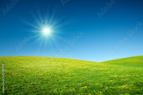 Spring landscape background with bright sun and green grass field.