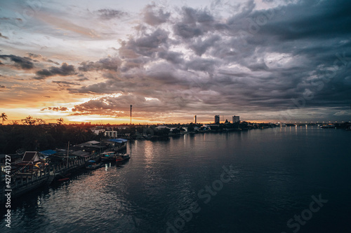 Panorama Cityscape at sunset with large river at foreground and strom clouds at background in Thailand.