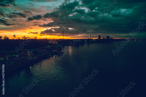 Panorama Cityscape at sunset with large river at foreground and strom clouds at background in Thailand.