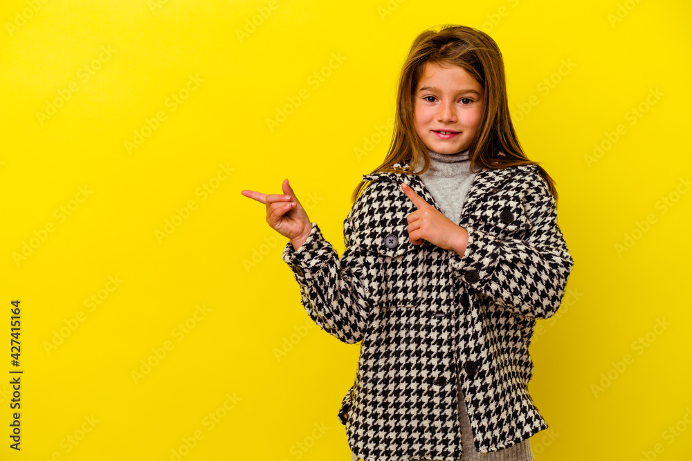 Little caucasian girl isolated on yellow background shocked pointing with index fingers to a copy space. Little caucasian girl isolated on yellow background shocked pointing with index fingers to a copy space.