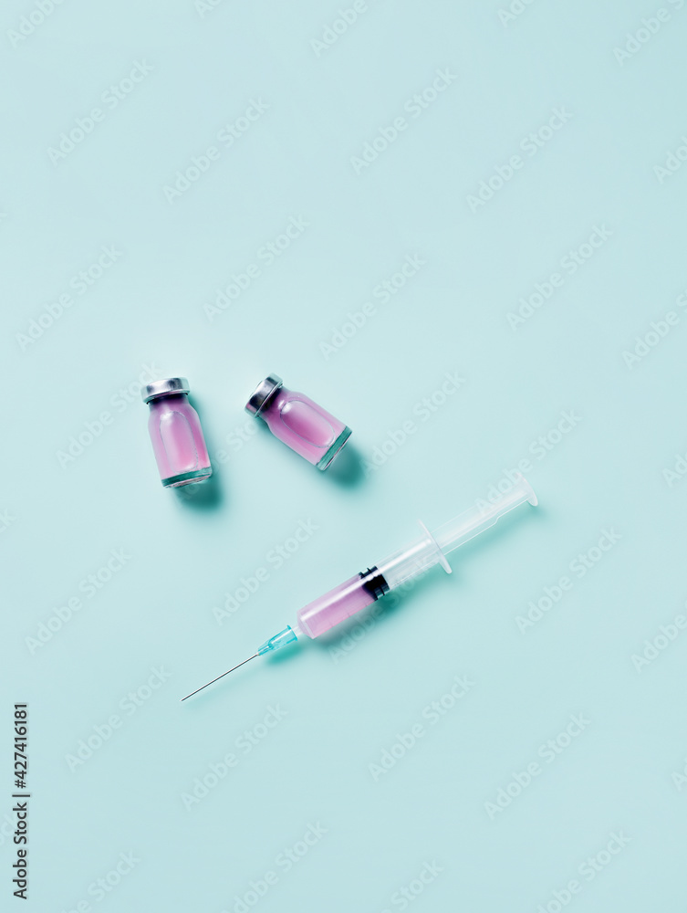 Syringe and vaccine bottle on neon background. Creative mass vaccination concept. Covid-19, influenza or flu global pandemic immunization. Cosmetology or skin care and rejuvenation. Syringe and vaccine bottle on neon background. Creative mass vaccination concept. Covid-19, influenza or flu global pandemic immunization. Cosmetology or skin care and rejuvenation.