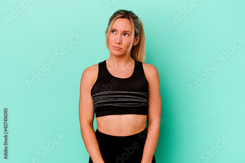 Young caucasian sport woman isolated on blue background confused, feels doubtful and unsure.