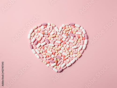 Pink pills arranged in a heart shape on pink background. Creative medicine, drugstore, healthcare and pharmacy concept. Production of medicine to treat illness with sincerity. Flat lay.