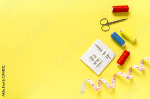 Flat lay of sewing accessories. Threads, needles, centimeter and scissors on yellow background, space for text