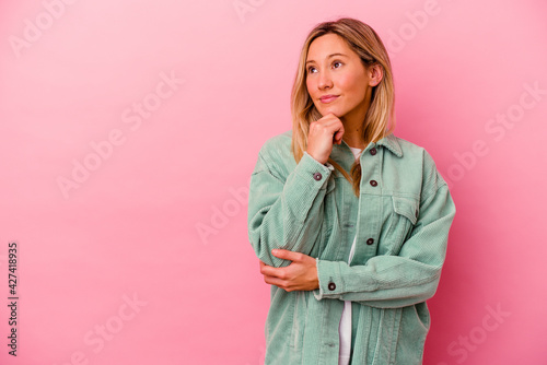 Young mixed race woman isolated on pink background looking sideways with doubtful and skeptical expression.
