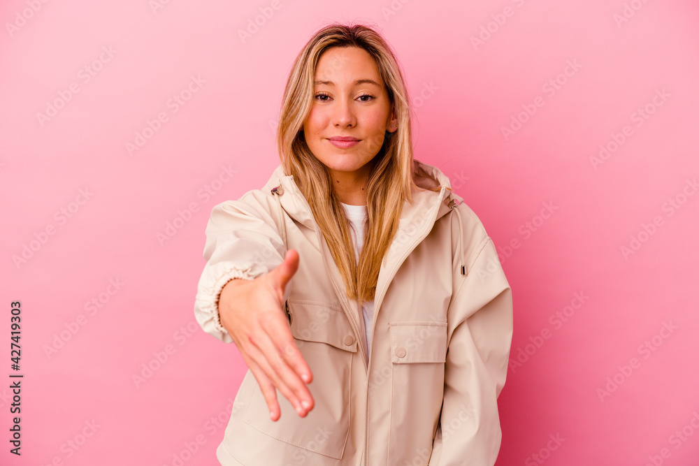 Young mixed race woman isolated on pink background stretching hand at camera in greeting gesture.