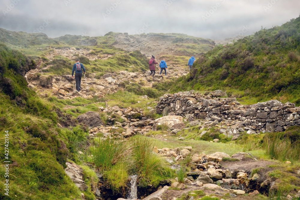 Tourists walking in a mountains, Croagh Patrick trail. Westport, county Mayo, Ireland. Mist over mountain peak.