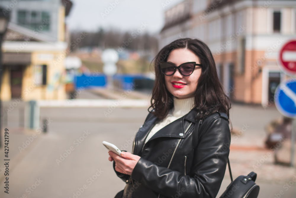 Obraz premium A beautiful hipster girl with a phone in her hands walks down the street