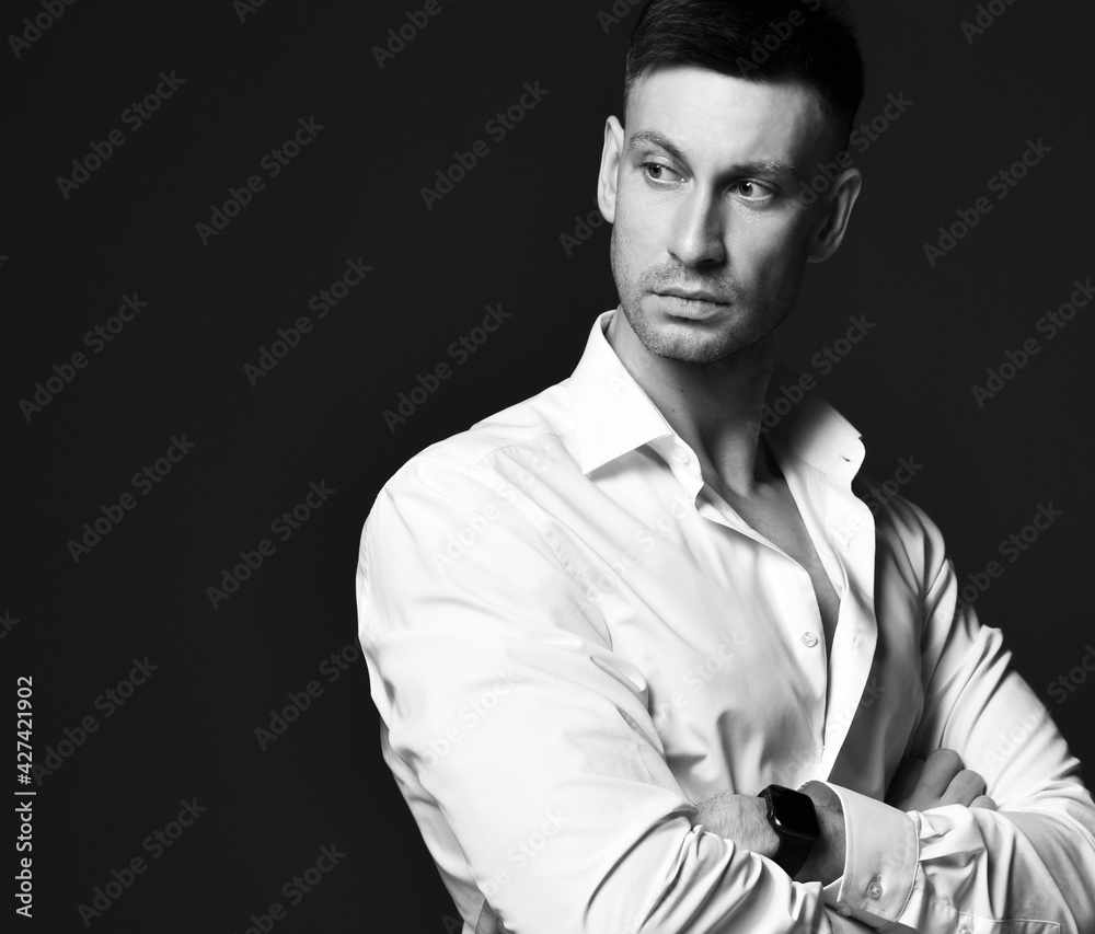 Portrait of distrustful cynical businessman in official white shirt standing with arms crossed at chest and looking back over shoulder over black background with copy space Portrait of distrustful cynical businessman in official white shirt standing with arms crossed at chest and looking back over shoulder over black background with copy space
