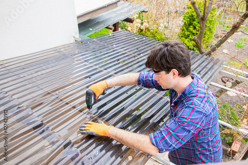 renovation of the roof made of polycarbonate sheets damaged by hail, handsome man repairing the roof, holes in polycarbonate sheets  photo