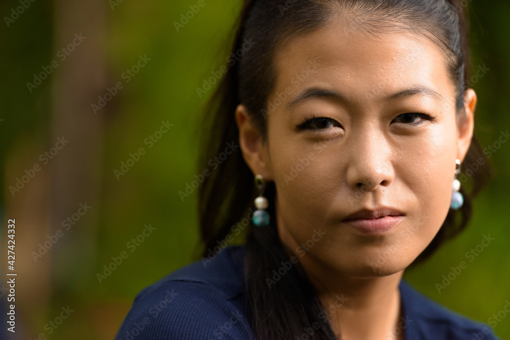Close-up portrait of beautiful rebel Asian woman face looking at camera outdoors