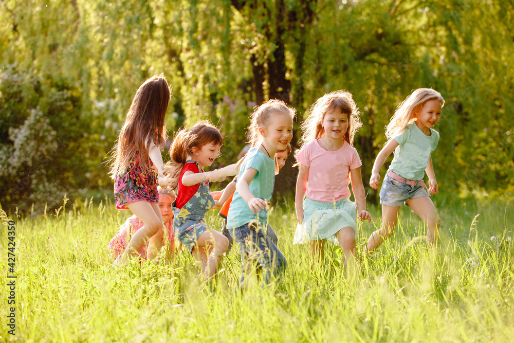 Obraz premium A group of happy children of boys and girls run in the Park on the grass on a Sunny summer day . The concept of ethnic friendship, peace, kindness, childhood