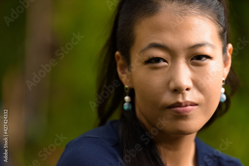 Close-up portrait of beautiful rebel Asian woman face looking at camera outdoors
