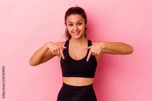 Young sport Indian woman isolated on pink background points down with fingers, positive feeling. © Asier