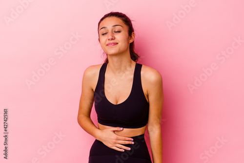 Young sport Indian woman isolated on pink background touches tummy  smiles gently  eating and satisfaction concept.