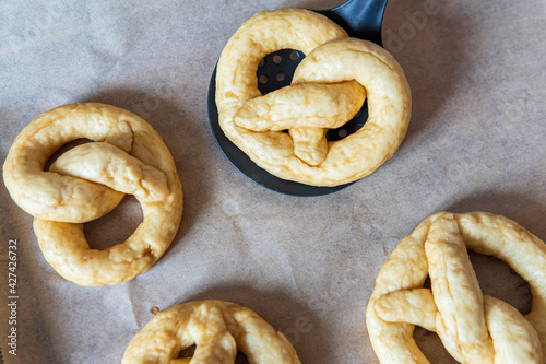 Homemade unbaked soft pretzel on a strainer spoon after being shortly cooked in water. Gluten free dough for savory delicious pastry with a knot. More pretzels in the background on a baking sheet.
