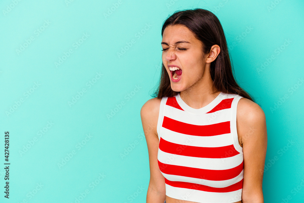 Young Indian woman isolated on blue background shouting very angry, rage concept, frustrated. Young Indian woman isolated on blue background shouting very angry, rage concept, frustrated.