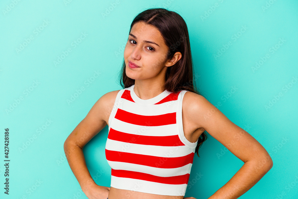 Young Indian woman isolated on blue background frowning face in displeasure, keeps arms folded. Young Indian woman isolated on blue background frowning face in displeasure, keeps arms folded.