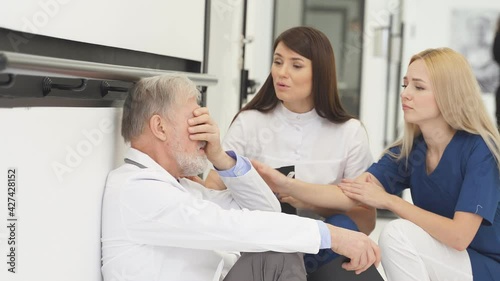 Group of doctors calm down sad colleague sitting on floor in corridor of hospital, try to help, have talk, wearing white medical coats.