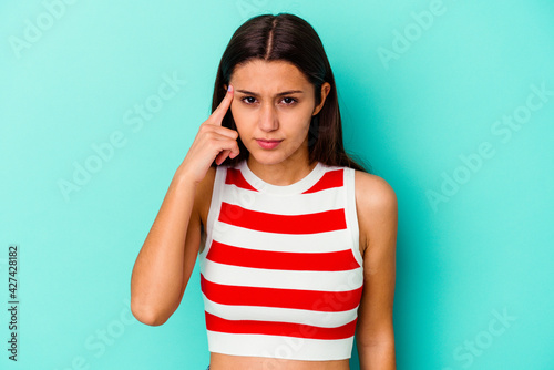 Young Indian woman isolated on blue background pointing temple with finger, thinking, focused on a task.