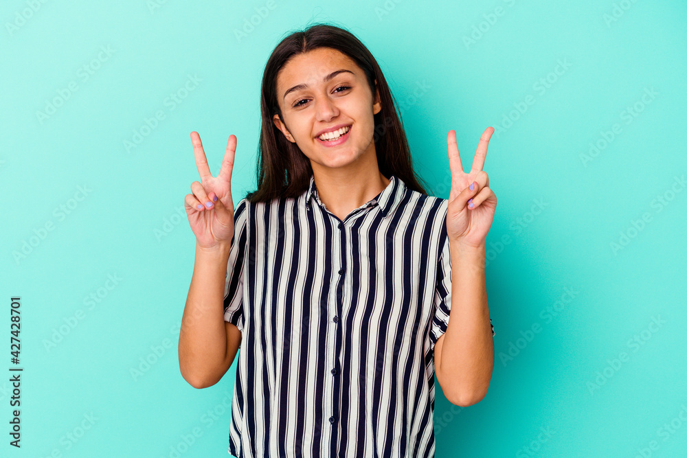Young Indian woman isolated on blue background showing victory sign and smiling broadly.