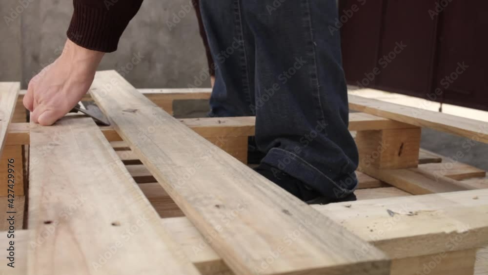 A young man disassembles a pallet. A wooden pallet, garden furniture. A man rips off the boards to make a table. Cheap DIY master eco-friendly wasteless with their own hands can't hard tear off A young man disassembles a pallet. A wooden pallet, garden furniture. A man rips off the boards to make a table. Cheap DIY master eco-friendly wasteless with their own hands can't hard tear off