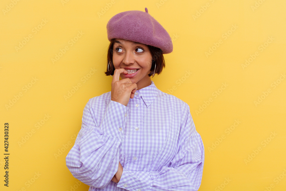 Young mixed race woman wearing a beret isolated on yellow background relaxed thinking about something looking at a copy space. Young mixed race woman wearing a beret isolated on yellow background relaxed thinking about something looking at a copy space.