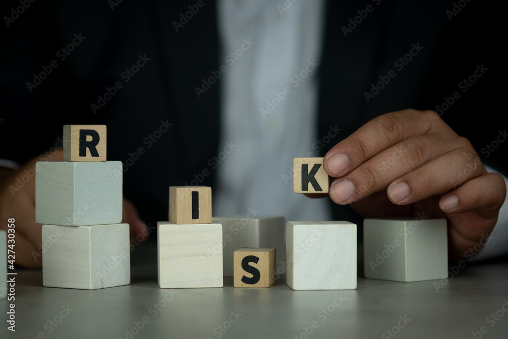 Businessman in suit holding of K wood block and removed with the word RISK. The concept of reducing risks and financial risk assessment Businessman in suit holding of K wood block and removed with the word RISK. The concept of reducing risks and financial risk assessment