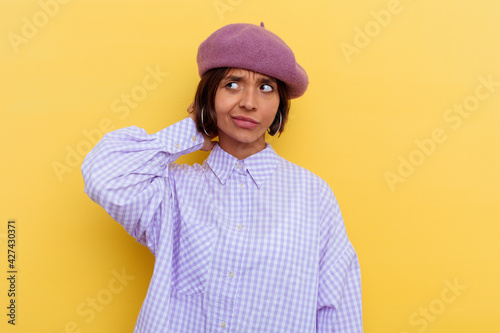 Young mixed race woman wearing a beret isolated on yellow background touching back of head, thinking and making a choice.