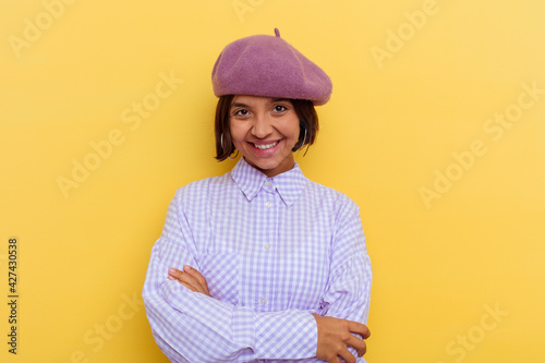 Young mixed race woman wearing a beret isolated on yellow background who feels confident, crossing arms with determination.