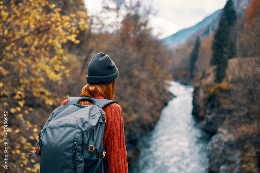 woman hiker with a backpack on her back near a mountain river in nature, back view