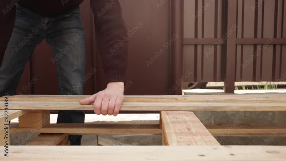 A young man lays wooden boards on the base for the table. Garden cheap furniture with your own hands. DIY eco-friendly waste master A young man lays wooden boards on the base for the table. Garden cheap furniture with your own hands. DIY eco-friendly waste master