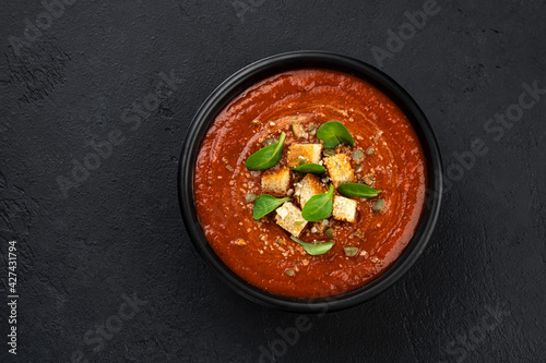 Bowl of tomato soup on black background, top view