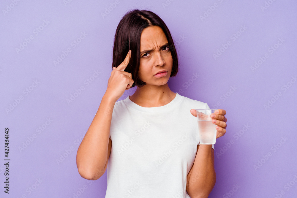 Young mixed race holding a glass of water isolated on purple background pointing temple with finger, thinking, focused on a task. Young mixed race holding a glass of water isolated on purple background pointing temple with finger, thinking, focused on a task.