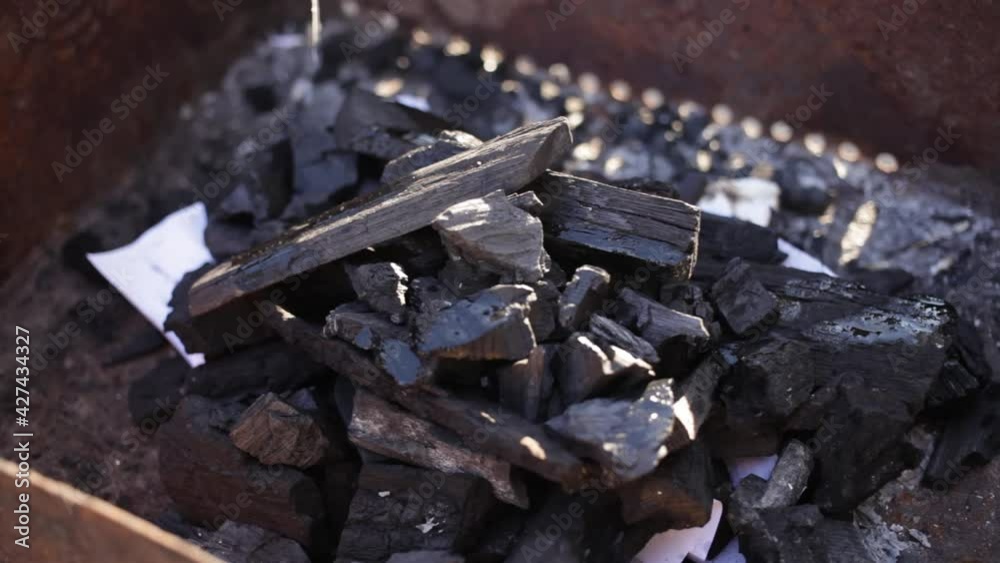 A young man lights a fire with paper matches and coals. Metal grill. Rest in nature, patio Bonfire for cooking barbecue a means of ignition A young man lights a fire with paper matches and coals. Metal grill. Rest in nature, patio Bonfire for cooking barbecue a means of ignition