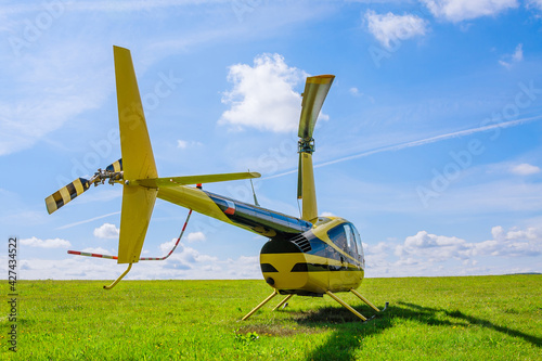 Modern small light helicopter on a grassy field against the blue sky.