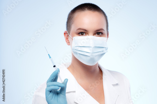 Short-haired woman doctor in mask holding syringe with medication