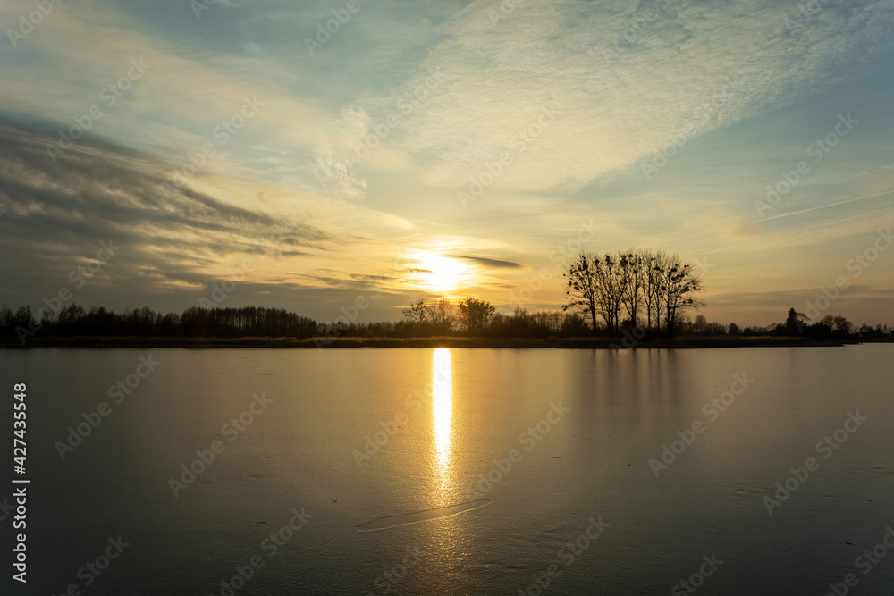 Sunset over a frozen lake with trees on the shore