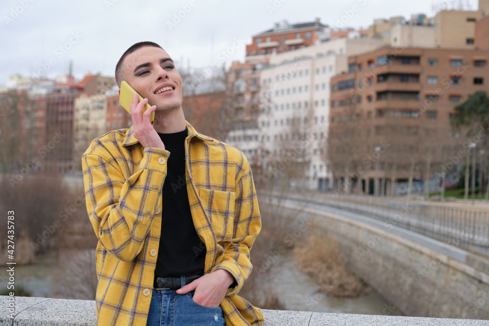 Fototapeta premium Young non binary person speaking on a smartphone laughing. Make up androgynous person.