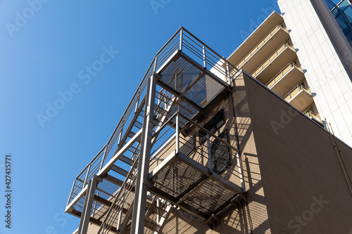 Modern fire escape staircase on the wall of a multi-storey building against a blue sky